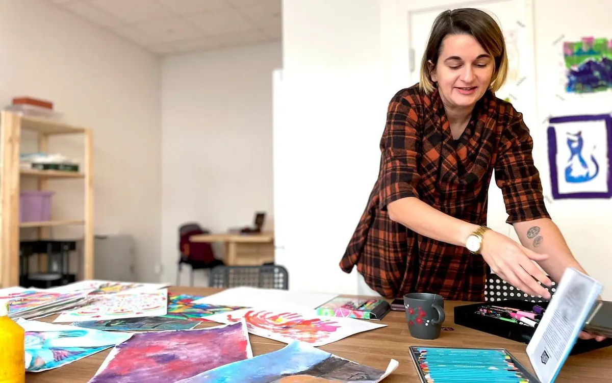 Lorena at The Stress Less Pencil studio in Kungälv, beside a table of colourful paintings and art supplies.