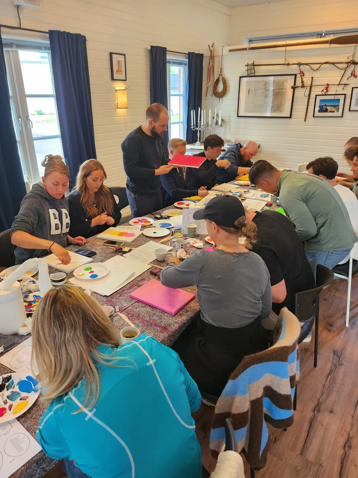 Deltagare målar tillsammans vid ett stort bord under ett kreativt teamevent.