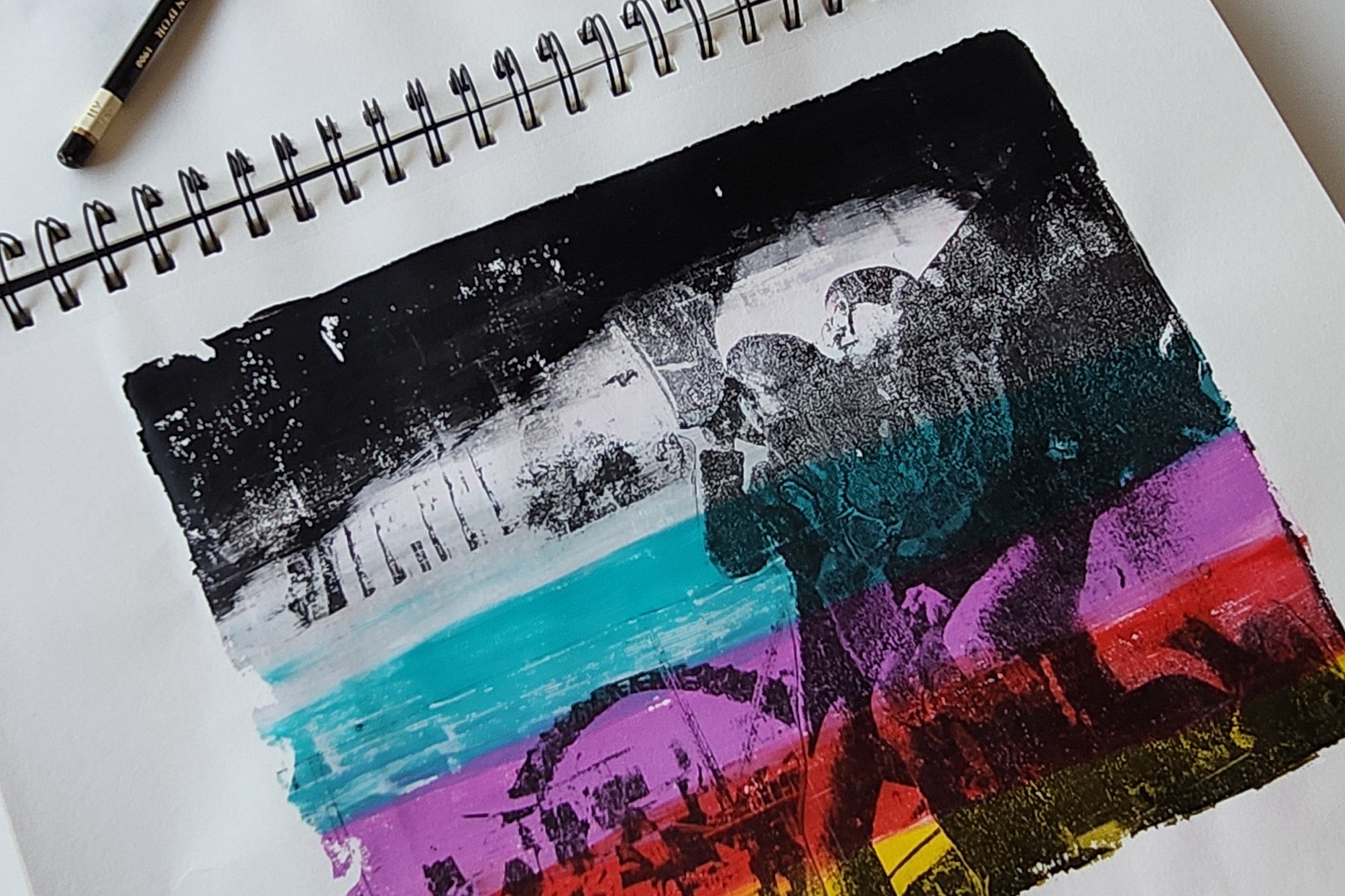 A printed artwork featuring layered print techniques with various colors, including black, blue, purple, and yellow, on a white background. A pencil and a pencil lead are also visible on the side.