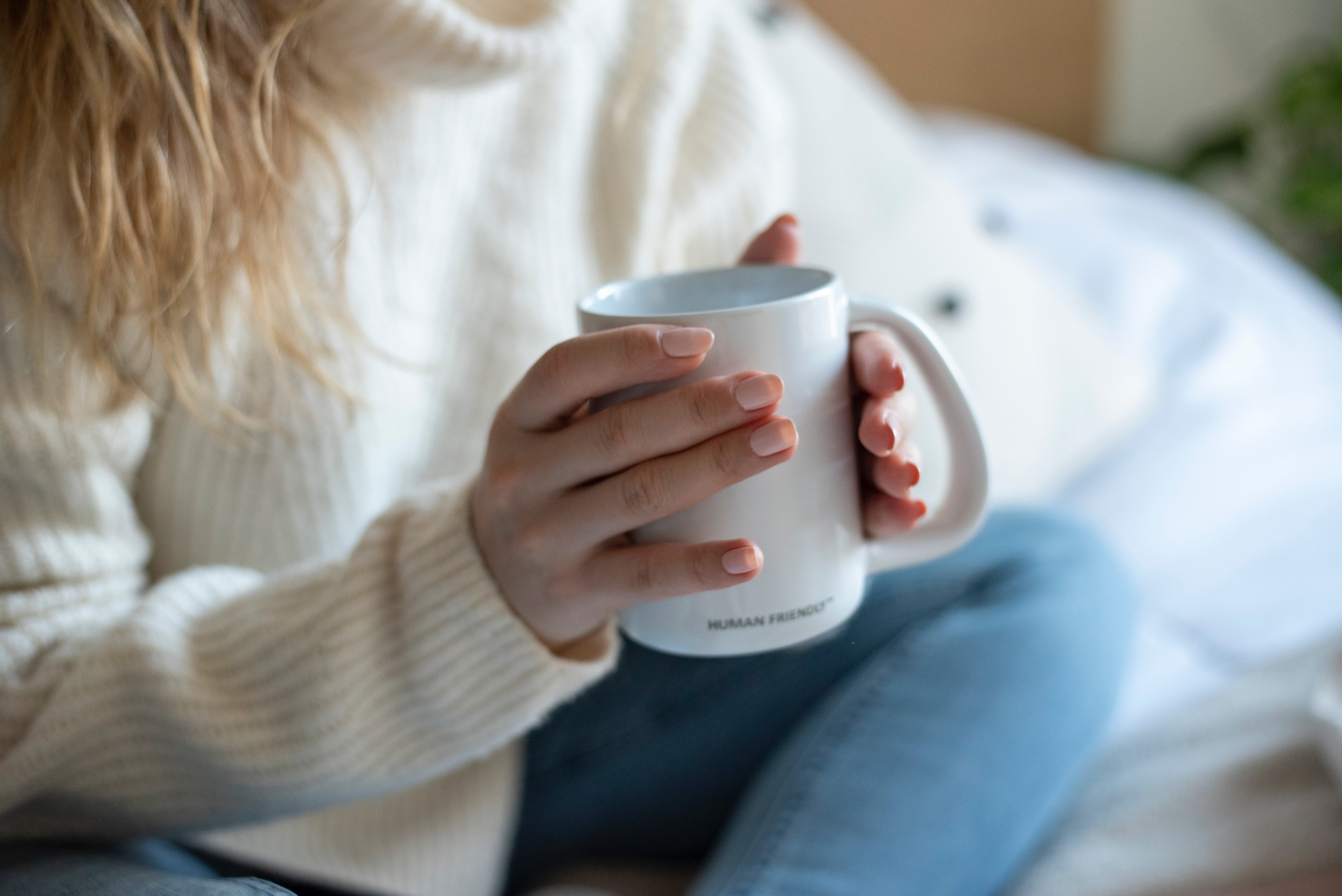a woman in jeans and a comfy sweater holding a cup